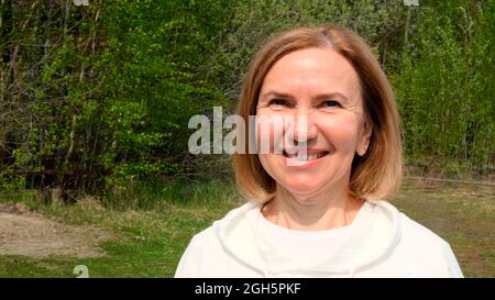Schöne reife Frau Gesicht. Dame mit mittlerem Erwachsenenalter, die im Freien lächelt. Porträt einer Frau im Alter von 55-60 Jahren beim Entspannen im Garten. Stockfoto