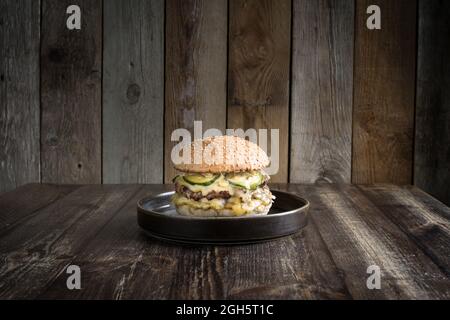 Köstlicher Hamburger mit heißem Fleisch und leckerem Käse auf schwarzem Teller auf Holztisch Stockfoto