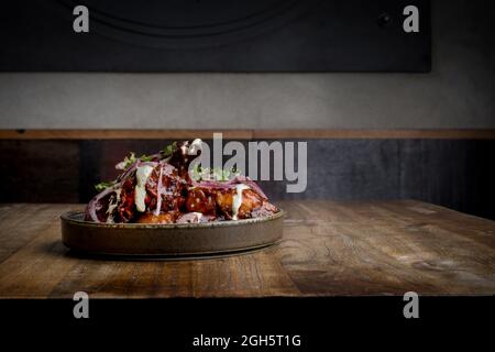 Leckere gegrillte Hähnchenflügel mit Barbecue-Sauce und Zwiebeln, serviert auf dem Holztisch im Restaurant Stockfoto