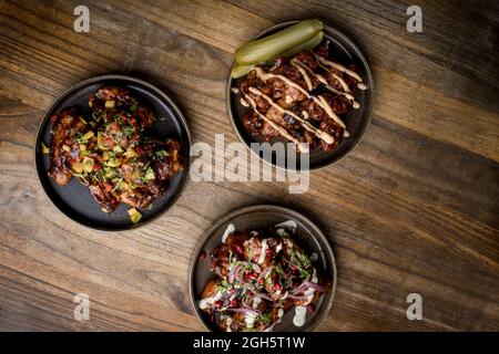 Set von köstlichen gegrillten Hähnchenflügeln in BBQ-Sauce mit Gemüse auf runden Tellern serviert und auf Holztisch im Restaurant platziert Stockfoto