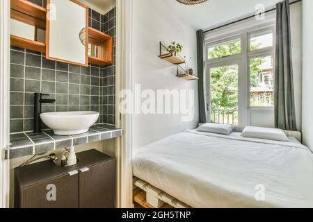 Interieur von kleinen hellen Schlafzimmer mit Palettenbett in der Nähe von Fenster und Waschbecken in modernen Wohnung Stockfoto