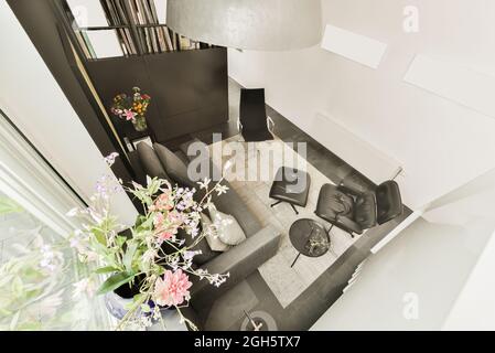 Von oben bequeme Ledersessel mit Fußstütze in der Nähe von Sofa in kleinen Lounge-Bereich mit Blumen in modernen Loft-Stil Wohnung eingerichtet Stockfoto