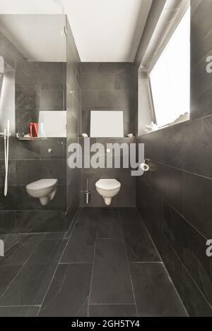 Interieur des modernen Badezimmers mit weißer Wand-Toilette und grauen Wänden und Boden in minimalem Stil gestaltet Stockfoto