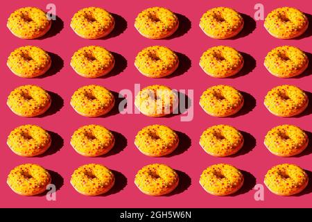 Draufsicht auf viele Donuts mit gelber Abdeckung und farbigen Kugeln auf rosa Hintergrund bedeckt Stockfoto