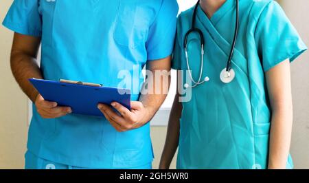 Anonyme männliche und weibliche Sanitäter lesen Bericht in der Zwischenablage, während sie im Korridor in der Klinik stehen Stockfoto