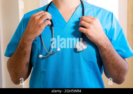 Crop anonyme männliche Medic in blauer Uniform und mit Stethoskop in der Klinik stehen Stockfoto