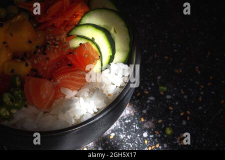 Im Restaurant wird ein großer asiatischer Poke mit Lachs und Reis und verschiedenen Gemüsesorten in einer Schüssel auf dem Tisch serviert Stockfoto