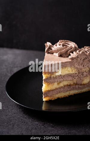 Von oben ein Stück köstlicher Trüffelschokoladenkuchen, serviert auf einem Teller auf einem schwarzen Tisch Stockfoto