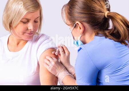 Nahaufnahme einer Ärztin, die eine medizinische Maske und Handschuhe trägt und eine Patientin mit dem Impfstoff gegen das Coronavirus impft. Stockfoto