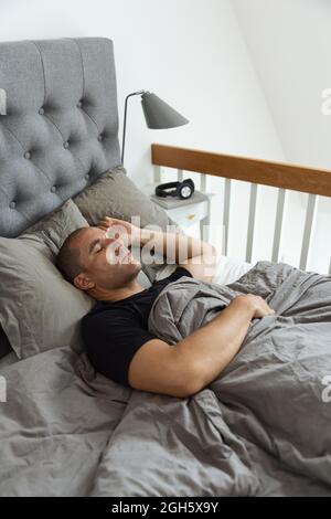Von oben ein friedlicher Mann, der im weichen Bett unter der Decke lag und morgens im Schlafzimmer schlief Stockfoto