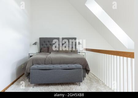 Komfortables Bett mit grauer Bettwäsche auf weichem weißen Teppich in einem kleinen Schlafzimmer im minimalistischen Stil im Haus Stockfoto