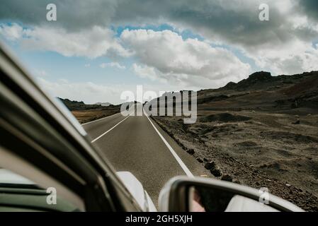 Fahrzeug, das an bewölktem Tag auf asphaltierter Straße durch arges vulkanisches Gelände in der Natur von Fuerteventura, Spanien, fährt Stockfoto