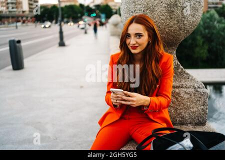 Positive afroamerikanische Frau mit Dreadlocks sitzen mit Kaffee zu Gehen Sie in Papierbecher auf Holzbank im städtischen Bereich Und wegschauen Stockfoto