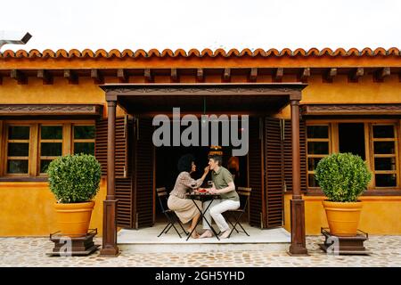 Seitenansicht einer schwarzen Frau, die den Mann mit Erdbeere fütterte, während sie am Tisch auf der Terrasse der Hütte saß und am Wochenende ein romantisches Date genoss Stockfoto