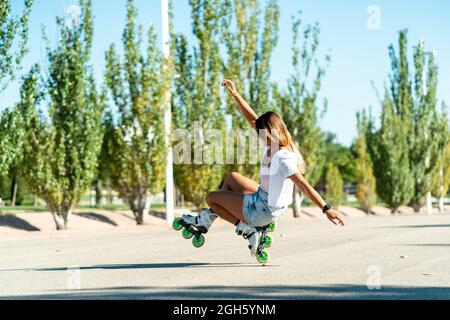 Seitenansicht der frauentauchten Frauen in Rollerblades und zeigt einen Wheelie-Trick mit einem Bein, während sie im Sommer in der Stadt unterwegs sind Stockfoto