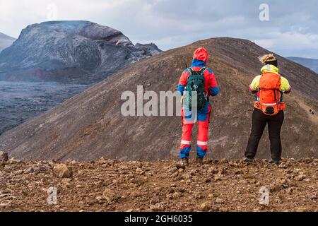 Wanderer stehen auf dem Berg gegen den Fagradalsfjall mit Lava und Rauch unter bewölktem Himmel in Island Stockfoto