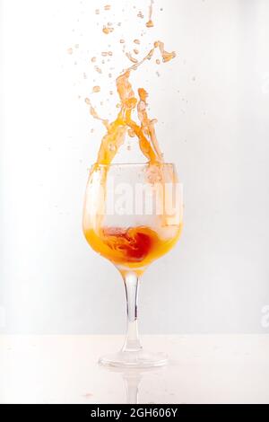 Erfrischender orangefarbener Cocktail, der im Studio auf grauem Hintergrund in einem glänzenden Glaskelch spritzt Stockfoto