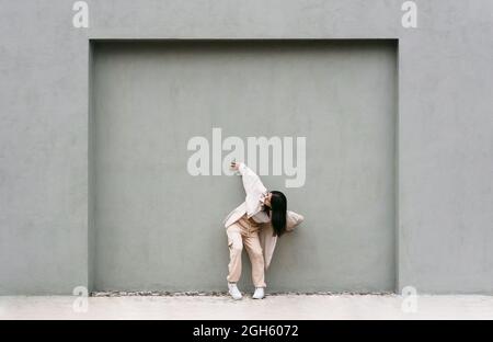 Energische Tänzerin, die sich in der Stadt bewegt und aufführt, während sie sich an einer grauen Wand lehnt Stockfoto