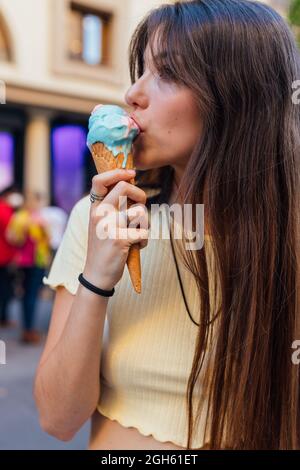Crop junge weibliche leckt leckeres Eis in Waffelkegel in der Stadt auf verschwommenem Hintergrund Stockfoto