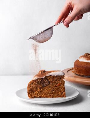 Crop unkenntlich Person mit Sieb bestreuen leckere Karotten Kuchen Stück mit gemahlenem Zimt auf hellem Hintergrund Stockfoto