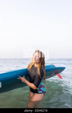 Eine positive, reife Frau mit durchbohrter Nase und Kopfhörern, die Sportkleidung trägt und dabei die Kamera anschaut, während sie während des Trainings auf dem Sportplatz steht Stockfoto