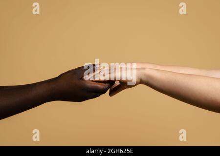 Seitenansicht der Ernte unkenntlich multiethnischen Weibchen halten Hände auf beigem Hintergrund im Studio Stockfoto