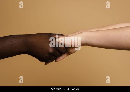 Nahaufnahme von nicht erkennbaren multiethnischen Frauen, die im Studio auf beigem Hintergrund die Hände halten Stockfoto
