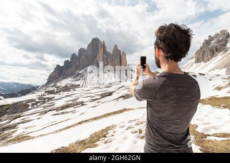 Rückansicht eines anonymen Wanderers, der während des Trekkings in den Dolomiten ein Bild von verschneiten Hochebenen auf dem Smartphone gemacht hat Stockfoto