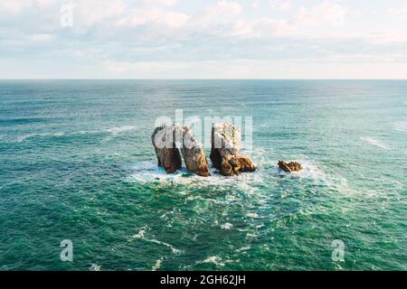 Von oben erstaunliche Meereslandschaft mit felsigen Formationen umgeben von plätscherndem türkisfarbenem Meerwasser unter blauem bewölktem Himmel in der Nähe von Liencros in Kantabrien Spanien Stockfoto