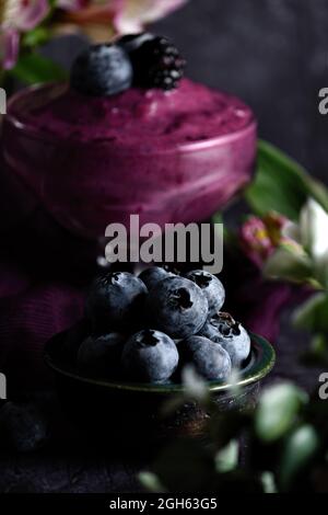 Nahaufnahme eines Stapels reifer Heidelbeeren in einer Schüssel, serviert auf einem schwarzen Tisch mit violettem Tuch Stockfoto