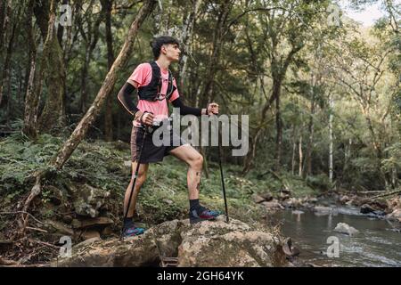 Männlicher Reisender mit Trekkingstöcken, die in der Nähe des Sees in Wäldern stehen Stockfoto