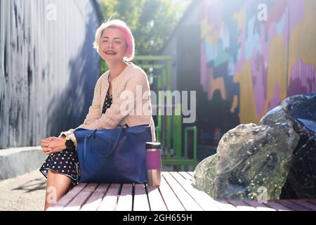 Seitenansicht einer trendigen alternativen Frau mit gefärbtem Haar, die auf einer Bank im Stadtgebiet der Stadt sitzt Stockfoto