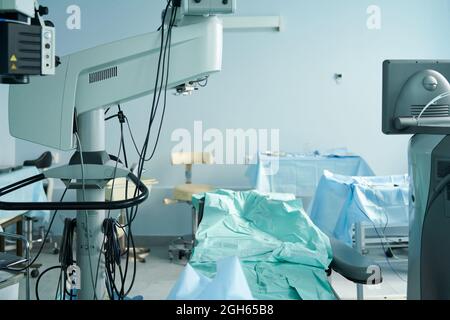 Medizinisches Bett mit Stoff zwischen Monitor und Operationsmikroskop an Tischen und Stuhl im Krankenhaus Stockfoto