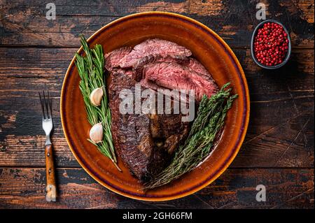 Gerösteter Aufhänger oder Onglet-Rinderfleischsteak in Scheiben auf einem rustikalen Teller mit Hackschnitzel. Dunkler Holzhintergrund. Draufsicht Stockfoto