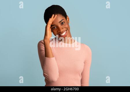 Porträt Einer Schüchternen Afroamerikanischen Frau, Die In Peinlicher Stimmung Lächelt Und Den Kopf Berührt Stockfoto