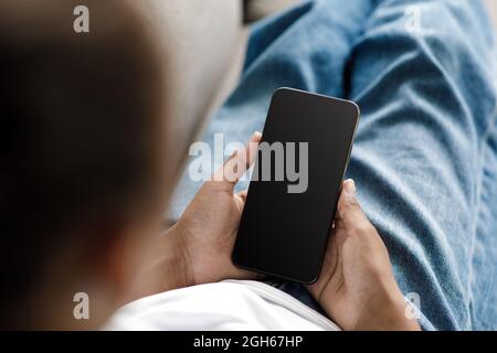 Junge schwarze Mädchen tippen auf Telefon mit leerem Bildschirm, Video ansehen oder auf dem Sofa zu Hause suchen Stockfoto