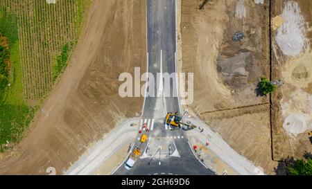 Oben, über Kopf auf einer kreisförmigen Straße, Kreisverkehr im Bau, Crew von Arbeitern auf der Baustelle, die am Straßenfundament neben dem aktiven T arbeiten Stockfoto