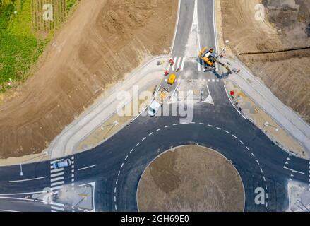 Oben, über Kopf auf einer kreisförmigen Straße, Kreisverkehr im Bau, Crew von Arbeitern auf der Baustelle, die am Straßenfundament neben dem aktiven T arbeiten Stockfoto