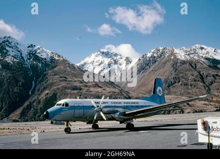 Ein Hawker Siddeley HS 748-Linienflugzeug der neuseeländischen Mount Cook Airlines auf dem Asphalt am Flughafen Queenstown im Jahr 1979 mit den Southern Alps im Hintergrund. Mount Cook Airline war eine regionale Fluggesellschaft, die 1920 gegründet wurde und ihren Sitz in Christchurch hatte. Später wurde es eine Tochtergesellschaft von Air New Zealand und 2019 wurde der Markenname in den Ruhestand verabschiedet. Dieses Flugzeug trägt den Namen ‘Aorangi’, ein Name der Maori. Auf dem Flugzeugheck befindet sich ein Bild der Mount Cook Lilie (Ranunculus lyallii), der größten Butterblume der Welt. Dieses Bild stammt von einem alten Kodak-Amateurfotograf mit Farbtransparenz – einem Vintage-Foto aus den 1970er Jahren. Stockfoto