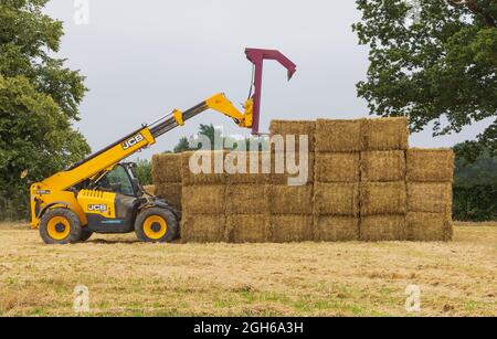 Mann, der einen Teleskoplader benutzt, um Strohballen auf einem Feld zu stapeln. VEREINIGTES KÖNIGREICH Stockfoto