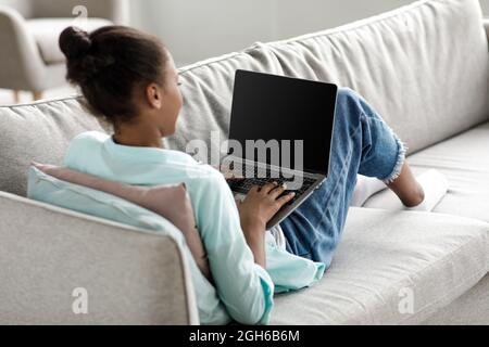 Teen african american Mädchen tippen auf Laptop mit leerem Bildschirm und Studie zu Hause innen Stockfoto