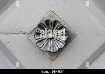 Klassischer Türknauf aus Metall mit Blumen-Optik auf einer hell gestrichenen Tür mit Rautenmustern Stockfoto
