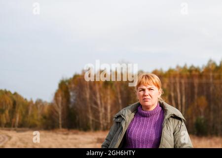 Unschärfe-Porträt von traurig deprimiert blonde 40er Jahre Frau zu Fuß in gelben Herbst Wald Natur Hintergrund. Frauen tragen einen lila Pullover. Herbstpark, Blätter. Stockfoto