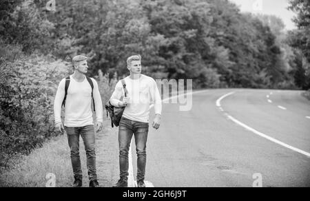 Gehen Sie in die Nähe des Stadtrandes. Reisende auf dem Weg. Freunde, die Wanderer auf Reisen anhalten. Unternehmen Freunde Reisende Anhalter auf Straße Natur Hintergrund. Beginnen Stockfoto