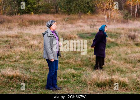 Unschärfe zwei Frauen auf einem Spaziergang in der herbstlichen Natur. Herbsthintergrund. Wunderschöne Parklandschaft. Zwei Frauen, die im Herbstwald entlang der Straße spazieren. Seite V Stockfoto