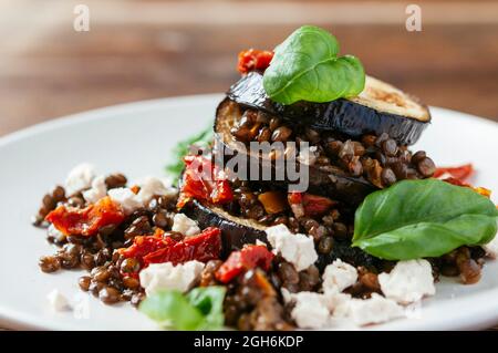 Auberginen-Linsen stapeln mit Sojakäse, getrockneten Tomaten und Basilikumblättern. Stockfoto