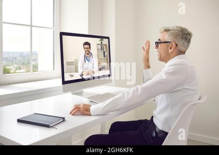 Leitender kaukasischer Geschäftsmann, der im Büro sitzt und per Videolink mit seinem Arzt spricht. Stockfoto