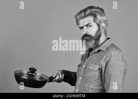 Wer kümmert sich um Ernährung. Kulinarik und Küche. Küchenutensilien. Gesundes Kochen. Kochen leckeres Gericht. Bärtiger Mann halten Bratpfanne. Kochen im Topf Stockfoto