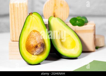 Hälften von reifen Avocado und Micro Green auf Holzpodium und Stände auf dem Tisch serviert, weißer Hintergrund, gesunde ölige Nahrung, Keto-Diät, Nahaufnahme Stockfoto