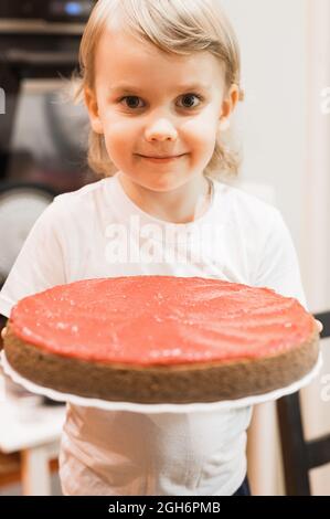 Porträt eines niedlichen kleinen glücklichen, ehrlichen kaukasischen fünfjährigen Jungen im weißen T-Shirt hält einen hausgemachten gebackenen Kuchen oder Kuchen in den Händen zu Hause Stockfoto